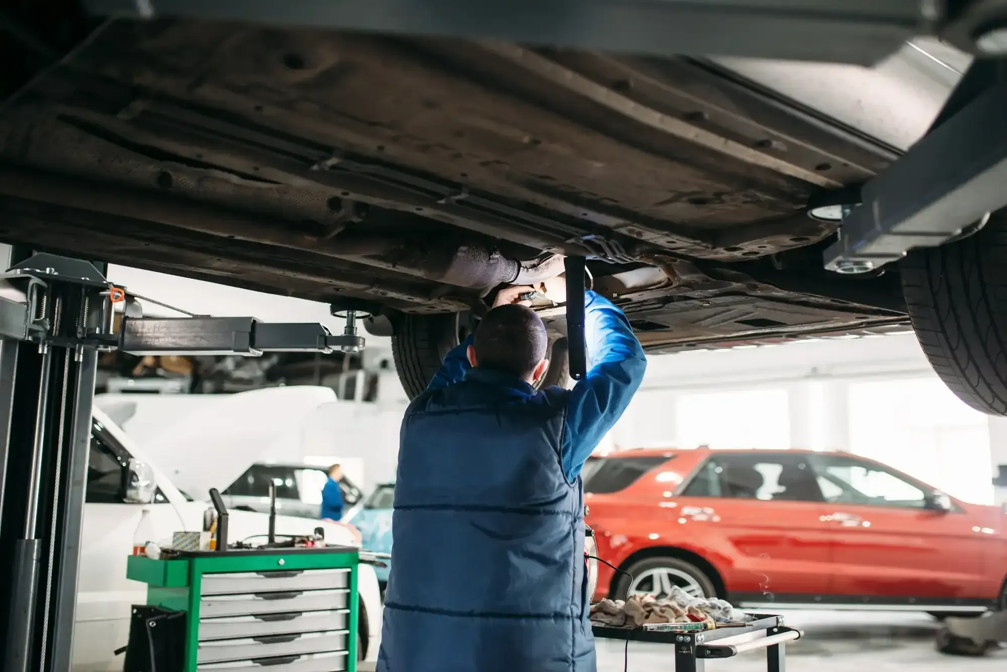 Mechanic inspecting the underside of a car on a lift during general auto repair
