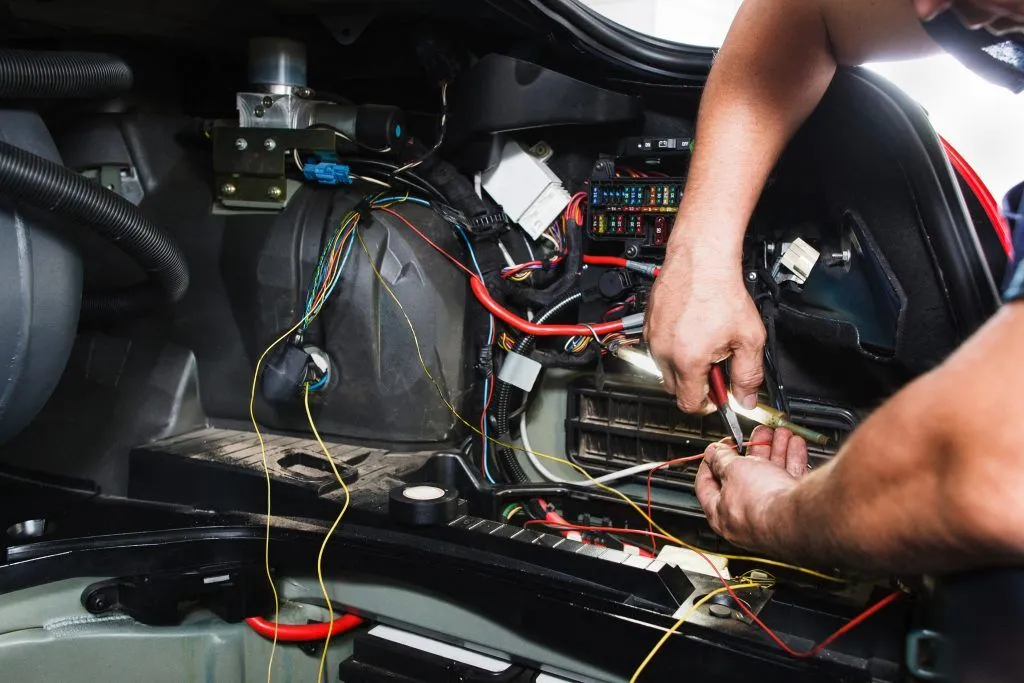 Technician repairing a car wiring harness with pliers during automotive electrical service